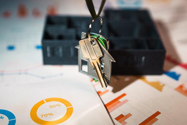 house-shaped-keychain-with-keys-hanging-over-real-estate-charts-and-graphs